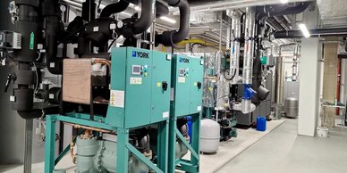 In einem modernen Technikraum stehen mehrere große Maschinen und Rohre, die für die Klimatisierung und Kühlung zuständig sind.