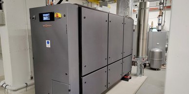 Eine moderne Heizungsanlage mit grauen Paneelen und einem digitalen Bildschirm, die in einem hellen Raum installiert ist.