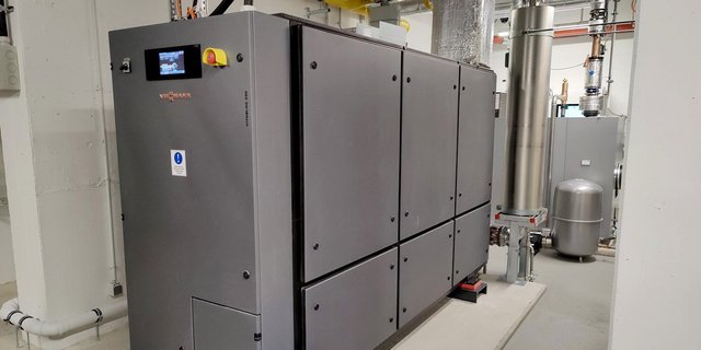 Eine moderne Heizungsanlage mit grauen Paneelen und einem digitalen Bildschirm, die in einem hellen Raum installiert ist.