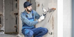 Ein Elektroniker der auf einem Rohbau die Kabel aus der Wand zieht