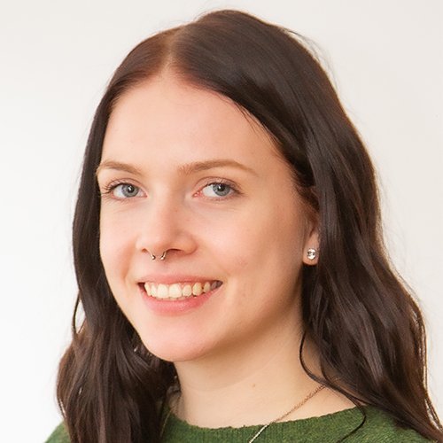 Mit einem warmen Lächeln und einem Nasenpiercing strahlt die Frau Selbstbewusstsein aus, während sie in die Kamera schaut.