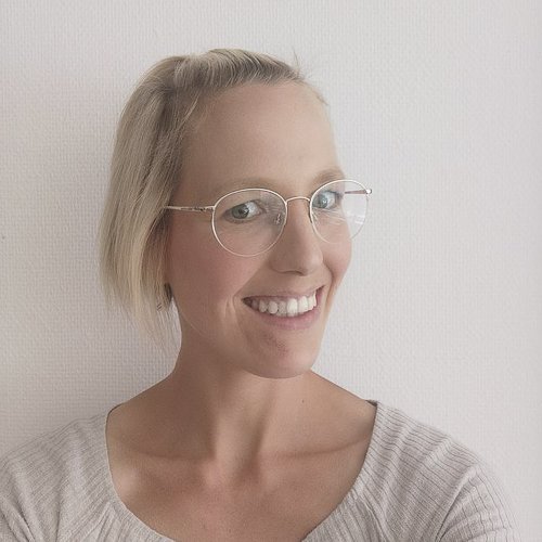 Die Frau trägt modische, runde Brillen und hat einen freundlichen Ausdruck, der Wärme und Offenheit ausstrahlt.