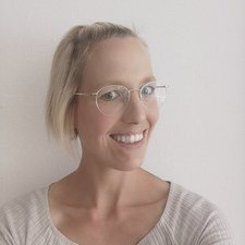 Die Frau trägt modische, runde Brillen und hat einen freundlichen Ausdruck, der Wärme und Offenheit ausstrahlt.