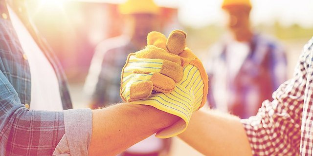 Zwei Arbeiter mit Handschuhen schütteln sich die Hände, um Teamgeist und Zusammenarbeit auf einer Baustelle zu zeigen.